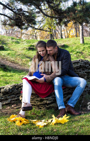 Young couple sitting in the park and reading. Woman is pregnant. Autumn season. Stock Photo