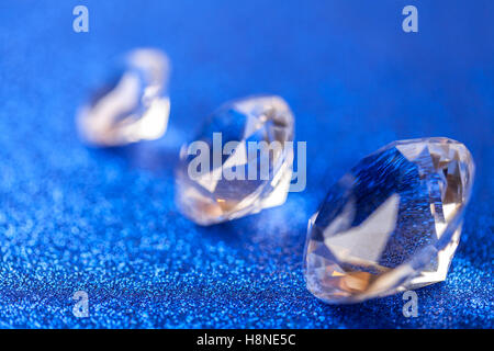 Three grand expensive diamonds laid on the diagonal on blue sparkling sequins background, macro . Big brilliant closeup. Stock Photo