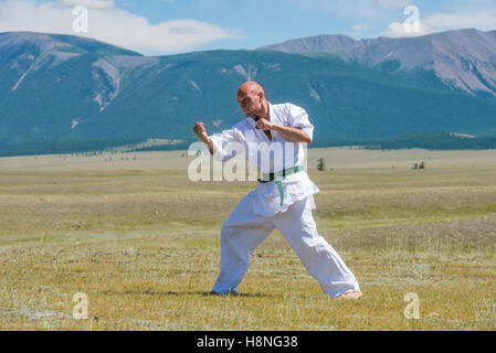 Man in white kimono and black belt training kung-fu, karate or aikido on mountain background. Stock Photo