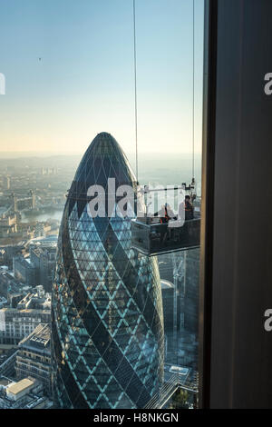 Workers suspended in a cable tethered cradle inspect the upper windows of the Heron Tower with the famous 'gherkin'. Stock Photo