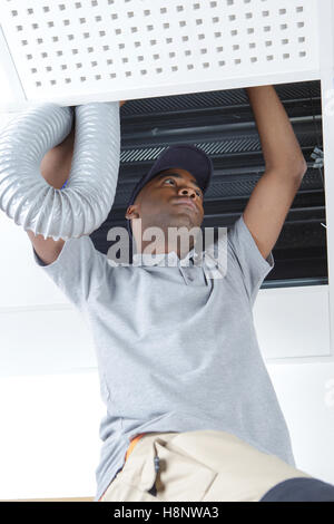 young african male electrician on stepladder fitting ventilation Stock Photo
