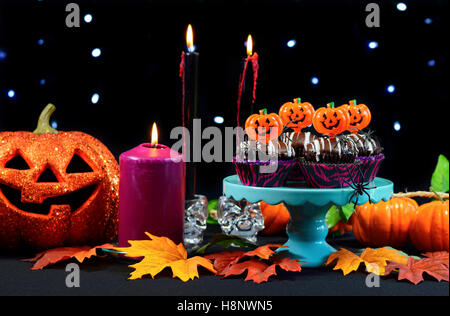 Halloween party table with chocolate cupcakes, spiders, pumpkins and candles against a black background with sparkling fairy lig Stock Photo