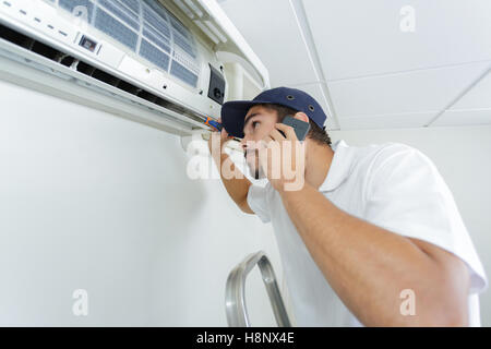 young handyman repairing air conditioning system calling for help Stock Photo
