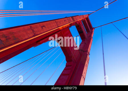 Low angle closeup detailed view of red Golden Gate Bridge tower and cables against a blue sky near San Francisco, California Stock Photo