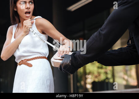 Irritated young woman screaming and fighting with robber why stealing her bag in the city Stock Photo