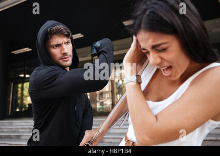 Man thief with gun attacking scared young woman on the street Stock Photo