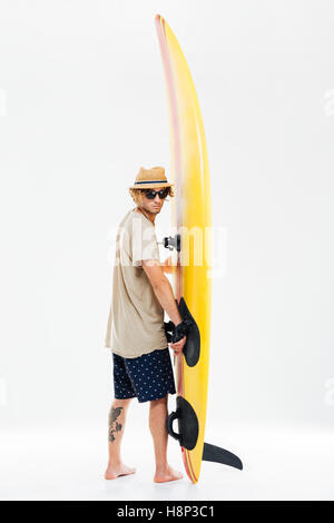 Back view a young surfer holding surfboard and looking over his shoulder isolated on the white background Stock Photo