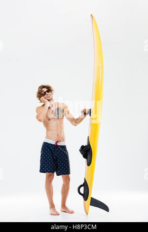 Smiling young sportsman holding surfboard and talking on mobile phone isolated on the white background Stock Photo