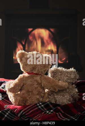 Two scruffy teddy bears sitting by the fire on a tartan blanket Stock Photo