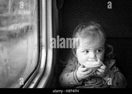 Cute innocent little girl traveling by train in England eating a mince pie at Christmas time Stock Photo