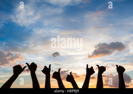 Silhouette of many people with thumbs up, symbol of like, satisfaction and agreement, sky background Stock Photo