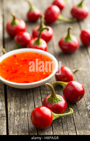 Red chili peppers and chili sauce on old wooden table. Stock Photo