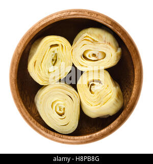 Artichoke hearts in wooden bowl over white. Cooked, canned flower buds of the globe artichoke, Cynara cardunculus var. scolymus. Stock Photo
