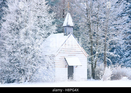 Small woody chapel in frozen snowy forest. Stock photo captured in Bavarian Alpine rural region Allgaeu Stock Photo