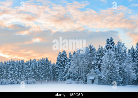 Small wooden chapel in snowbound frosty forest under morning sunrise sky. Amazing idyllic winter landscape Stock Photo