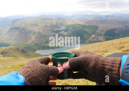 Model relaxing with a warm drink, enjoying the view from Helvellyn summit. Looking over Thirlmere lake and the mountains beyond. Stock Photo