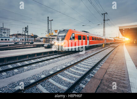 Modern high speed red commuter train at the railway station at colorful sunset. Railroad with vintage toning. Train at railway Stock Photo