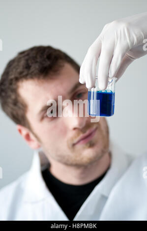 Chemist holding a measuring cup filled with a blue liquid Stock Photo