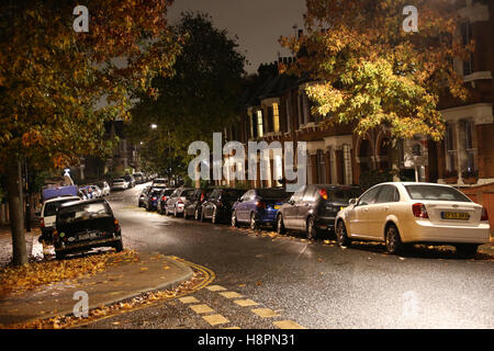 Autumn leaves cover the pavements and streets in a typical South London street after dark on a wet night Stock Photo