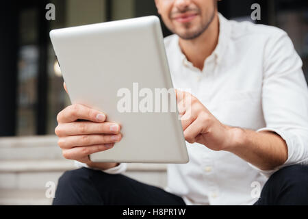 Closeup of young businessman holding and using tablet outdoors Stock Photo