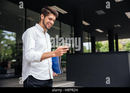 Cheerful handsome young businessman using smartphone in the city Stock Photo