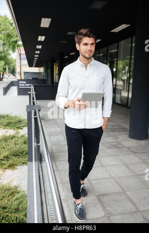 Handsome young businessman walking and using tablet in the city Stock Photo