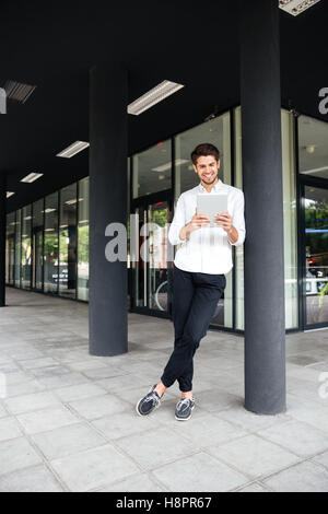 Happy young businessman standing near business center and using tablet Stock Photo