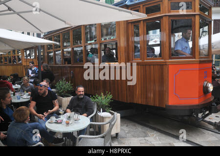Tourists on the tram that runs from Soller to the port of Soller. Here it travels through the town, past cafes and bars. Stock Photo