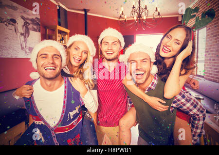 Composite image of portrait of men wearing christmas wearing giving women piggyback rides Stock Photo