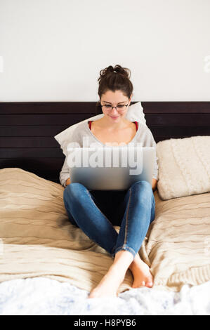 Beautiful young woman sitting on bed, working. Home office. Stock Photo