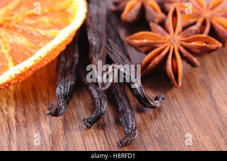 Fresh fragrant vanilla sticks pods, star anise and slices of dried orange on wooden board, seasoning for cooking or baking Stock Photo