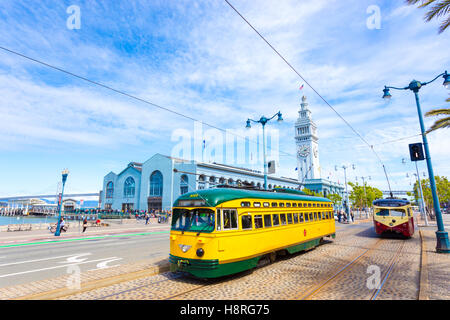 Two vintage F market streetcars pass in front of Ferry Building on Embarcadero and Bay Bridge in background on a sunny, blue sky Stock Photo