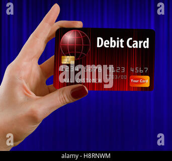 A female hand holds a debit card that is red and black. in front of a blue curtain. This is a photo illustration combining photo Stock Photo