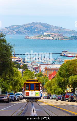 Approaching cable car full of tourists coming uphill with Angel and Alcatraz Island, bay water in background on Hyde Street Stock Photo