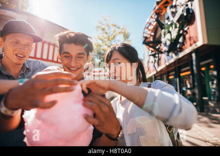 Young men and woman sharing cotton candy floss at fairground. Group of friends eating cotton candy in amusement park. Stock Photo