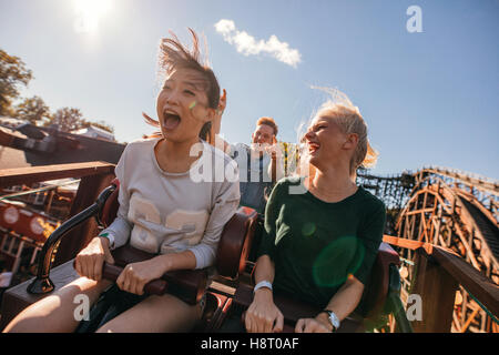 Young friends on thrilling roller coaster ride. Young women and men having fun at amusement park. Stock Photo