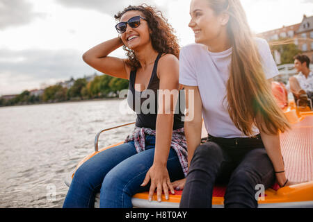 Outdoors shot of two female friends sitting in front pedal boat. Teenage friends relaxing on pedal boat in lake Stock Photo