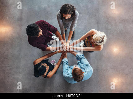 Young people putting their hands on top of each other symbolizing unity and teamwork. Diverse group of students stacking their h Stock Photo