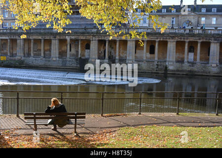Woman on park bench on Riverside Walk looking across River Avon to Grand Parade, Bath, Somerset, England Stock Photo