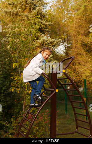 Cute little girl climbs the stairs to the playground in autumn park. Stock Photo