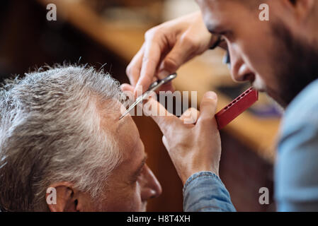 Hair dresser cutting bang of senior man Stock Photo