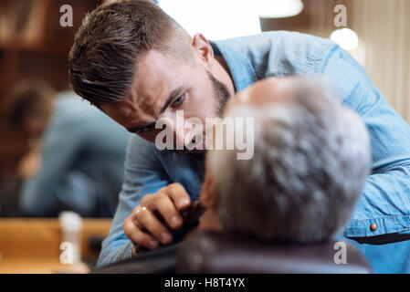 Attractive barber shaving beard of senior man Stock Photo