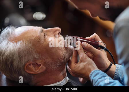 Old man getting his beard shaved by barber Stock Photo