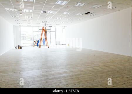 Team of workers electricians are using the wooden ladders to complete office ceiling with air duct and lamps. Stock Photo