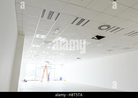 Team of workers electricians are using the wooden ladders to complete office ceiling with air duct and lamps. Stock Photo