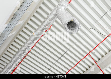 Ventilation pipes in silver insulation material and fire sprinkler on red pipe are hanging from the ceiling inside new building. Stock Photo