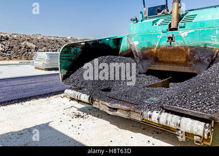 Front view on asphalt laying machine full of fresh asphalt at road construction site. Hot asphalt is spreading from paver machin Stock Photo