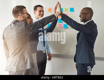 Group of business executives congratulating each other as they stand grouped together in an office doing a high fives hand gestu