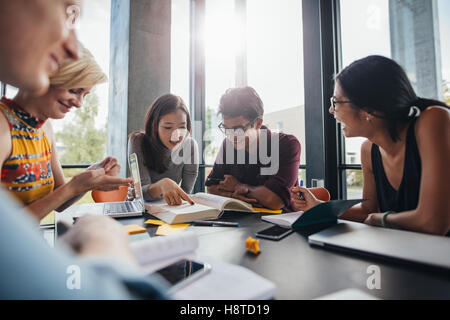 Young students sitting at a table in a library and reading books for their class assignment. university students doing group stu Stock Photo