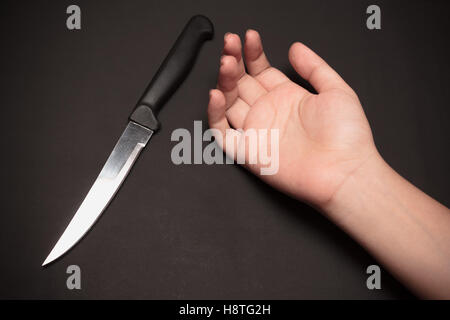 A sharp kitchen knife beside somebody's hand on dark background. This image was shot with single flash light bouncing technique. Stock Photo